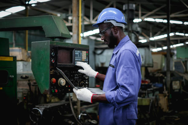 African american factory worker in using laptop and push buttons to test the machine operation after maintenance.