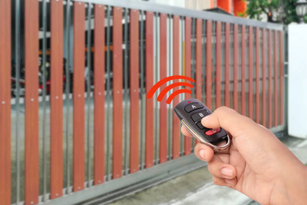 Female hand holding and showing remote control to open or close the automatic wooden gate with home blurred background. Security and save time concept.