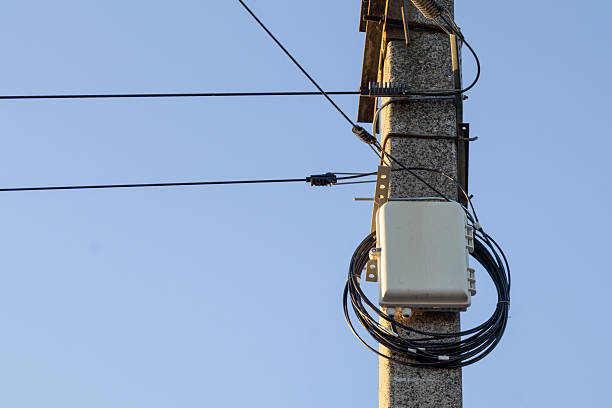 A utility pole stands tall with network cables and equipment attached. The clear sky provides a backdrop for this urban scene during the day.